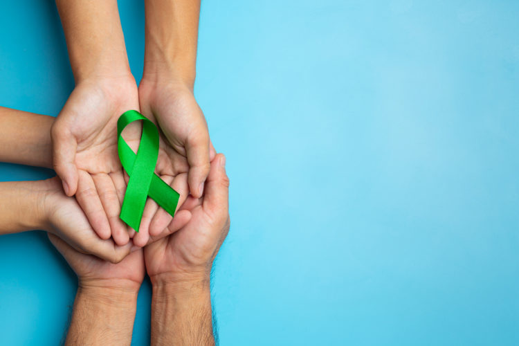 World Mental Health Day; green ribbon put in human's hands on blue background